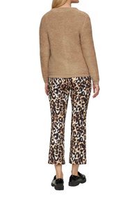 Beżowy sweter z dzianiny o teksturowanym wykończeniu, zestawiony z spodniami z szerokimi nogawkami w leoparda w kolorze kremowym, brązowym i czarnym, oraz czarnymi butami na platformie.