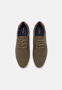 Chaussures à lacets marron et olive avec une tige texturée et des accents de talon contrastants en marron. Semelle en caoutchouc blanche, lacets plats.