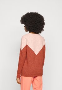 Dzianinowy sweter w kolorze rdzawym i jasnoróżowym z wzorem blokowym w kształcie litery V. Okrągły dekolt, długie rękawy i miękka faktura. Pokazany widok z tyłu.