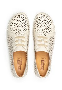 Zapatos de cuero color crema con un diseño perforado, cordones elásticos y una suela flexible. Presentan una textura suave y una plantilla de color marrón claro.
