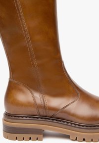 Botte en cuir marron hauteur genoux avec une finition lisse, des accents cousus et une semelle en caoutchouc avec un motif de grip texturé.