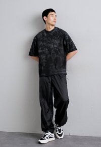 Zwart T-shirt met korte mouwen en een gestructureerd patroon, gecombineerd met losse zwarte broek en witte sneakers met zwarte accenten.
