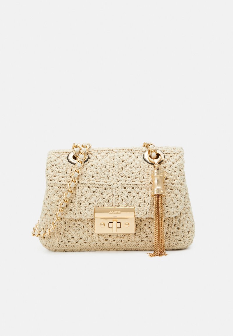 Sac à main crocheté de couleur crème avec bandoulière chaîne dorée, fermoir doré et pampille décorative dorée sur fond blanc.