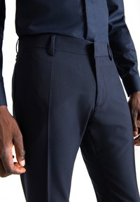 Pantaloni tailleur blu navy con una texture liscia, dotati di una vita e cuciture laterali sottili, progettati per una vestibilità formale.