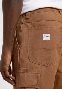 Pantalones cargo de trabajo en color marrón de Lee, con múltiples bolsillos, costuras reforzadas y una etiqueta de parche tejida. Tela duradera con un acabado texturizado.