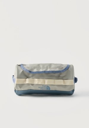 Borsa da toilette grigia e blu The North Face con tracolla beige e cerniera superiore, posata su uno sfondo bianco uniforme.