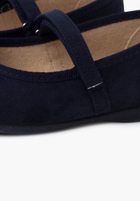 Zapatos planos de ante azul marino con punta redonda, tira única sobre el empeine y una suave plantilla beige. Tejido texturizado y diseño minimalista.
