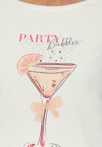 Witte T-shirt met een afbeelding van een cocktailglas, roze accenten, een schijfje citroen, bellen en de tekst "PARTY Bubbles" in verschillende lettertypen.