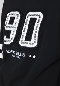 Felpa nera con grande numero "90" bianco decorato con borchie argentate e ricamo testurizzato. Include la scritta "Marc Ellis New York" in bianco sottostante.
