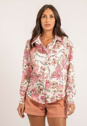 Chemise à manches longues à boutons en tissu léger, avec un motif floral aux accents roses, marron et bleu-vert, associée à un short beige.