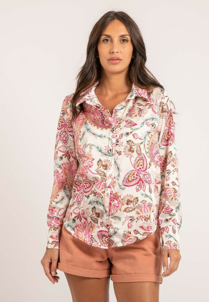 Chemise à manches longues à boutons en tissu léger, avec un motif floral aux accents roses, marron et bleu-vert, associée à un short beige.
