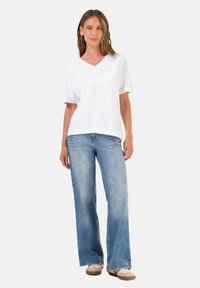 Top bianco a maniche corte con scollatura a V abbinato a jeans a gamba larga blu chiaro e sneaker beige. Design semplice; texture in cotone. Look minimalista.