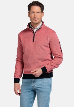 Rode sweatshirt met een ritskraag, zwarte accenten en een gestructureerde stof. Gecombineerd met lichtblauwe jeans, met een zijzak.