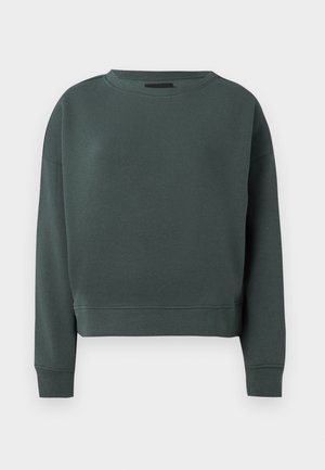 Tumši zaļš džemperis, izgatavots no gluda kokvilnas auduma maisījuma. Tam ir apaļa kakla izgriezums un ribota apkakle. Apgriezta dizaina ar minimālu šuvju detaļu.