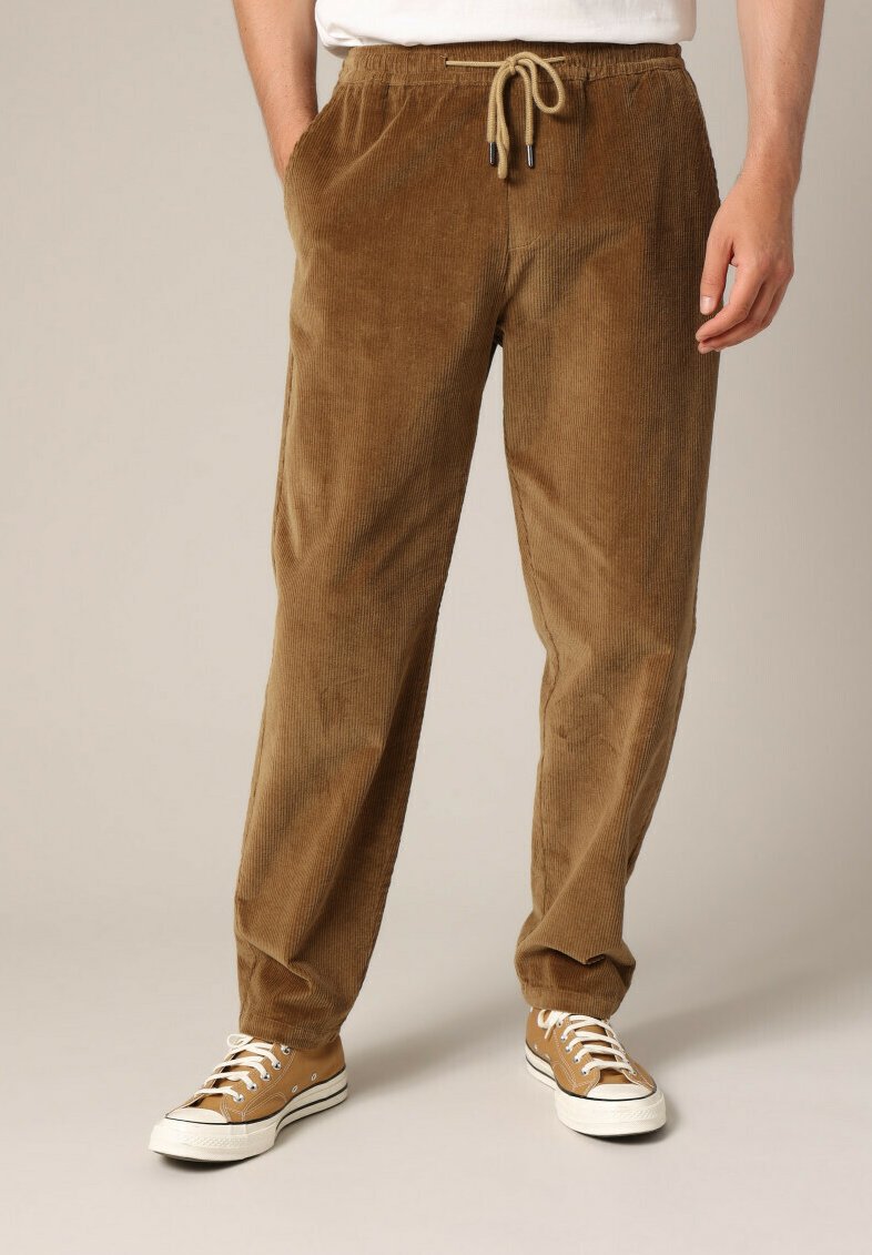 Bruine corduroy broeken met een elastische tailleband en trekkoord, voorzien van zijzakken en een ontspannen pasvorm, gecombineerd met beige sneakers.