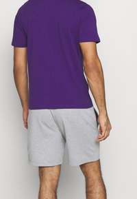 Fialové bavlněné tričko s krátkým rukávem, spárované se světle šedými sportovními šortkami. Měkká textura, minimalistický design a bez viditelných vzorů.