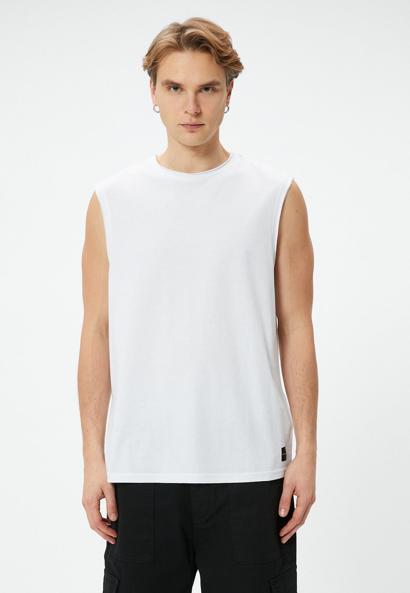 Vitt ärmlöst t-shirt av mjukt tyg, med rund hals och rak nederkant. Enkla design med minimal varumärkering längst ner.