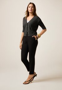 Cardigan grigio con maniche corte, scollo a V e dettagli con bottoni, abbinato a pantaloni neri aderenti e sandali neri con cinturini. Accessoriato con bracciali.