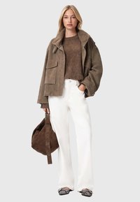 Bruine suede jas met een hoge kraag, een beige fuzzy trui eronder, witte broek en een bruine slouchy tas. Heeft een ontspannen pasvorm en minimale metalen details.