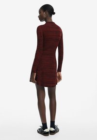 Abito rosso a maglia con maniche lunghe, dotato di un motivo testurizzato e uno spacco laterale. Abbinato a sneakers bianche e nere.