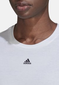 Camiseta blanca de algodón con un cuello redondo y un pequeño logo negro de Adidas en el pecho. Textura suave con un diseño casual.