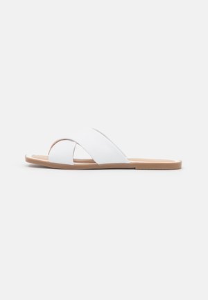 White slide sandals made of synthetic material, featuring a cross-strap design, flat base, and a light brown outsole.