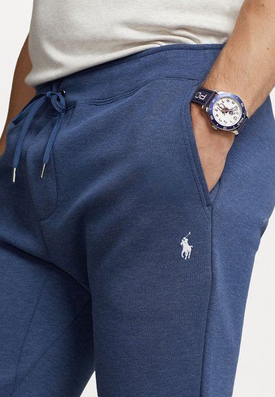 Ναυτικό μπλε βαμβακερές φόρμες με ρύθμιση κορδονιού στη μέση, πλαϊνές τσέπες και μικρό λευκό λογότυπο polo στο αριστερό πόδι. Λείος υφή, χαλαρός σχεδιασμός.