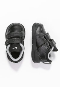 Černé boty pro batolata s texturovaným koženým svrškem, dvěma suchými zipy, šedým podšíváním a gumovou podrážkou. Obsahují malé bílé logo.