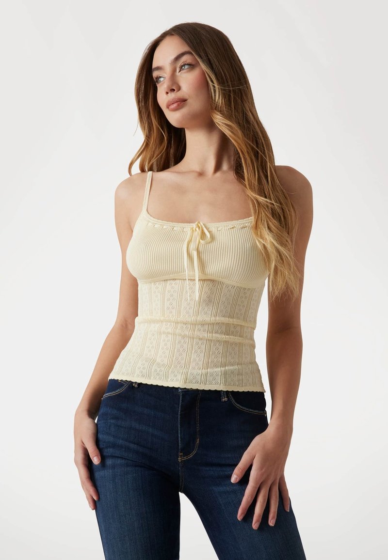 Top giallo a righe con spalline regolabili, caratterizzato da un dettaglio con cordoncino e una texture in pizzo a motivo in vita, abbinato a jeans scuri.