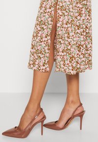 Escarpins à bouts pointus avec lanières arrière en cuir verni rose glossy, talon aiguille et panneau arrière texturé, assortis à une robe à motif floral.