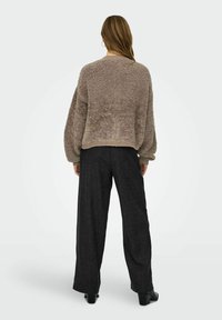 Puszysty, taupe sweter o luźnym kroju i prążkowanym wykończeniu, zestawiony z spodniami o wysokim stanie, szerokimi nogawkami, teksturowanymi i w ciemnym węglowym kolorze oraz na słupku.