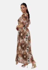 Robe longue à fleurs avec de grandes fleurs brunes et roses sur un fond clair. Tissu fluide avec des manches courtes et évasées, et taille cintrée.