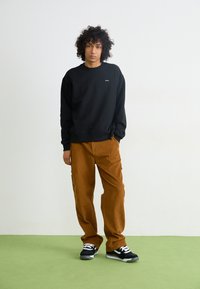 Zwarte sweatshirt met een ronde halslijn en omgeslagen mouwen, gecombineerd met een paar bruine corduroy broek met zijzakken en zwarte sneakers.