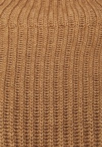 Neulottu villapaita pystyraidallisella neuloksella lämpimässä, vaaleanruskeassa sävyssä. Pintakuvio on paksu ja pehmeä, ja langan yksityiskohdat sekä tiukat silmukat erottuvat selvästi.