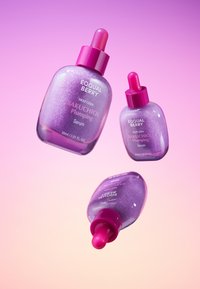 Trzy butelki serum plumping Equal Berry Bakuchiol, zawierające lśniący fioletowy płyn, różowe zakraplacze i smukłe, zaokrąglone kształty.