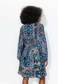 Robe à motifs floraux avec manches longues, présentant un mélange de couleurs bleu, sarcelle et bordeaux, en tissu doux, avec une jupe évasée.