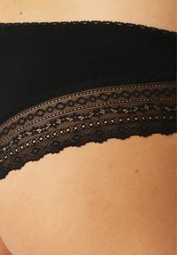 Schwarze Baumwollhipster-Unterwäsche mit einer zarten Spitze, die geometrische Muster entlang des Taillenbundes und der Beinöffnungen aufweist.