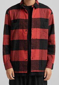 Camicia a quadri rossi e neri realizzata in tessuto strutturato, dotata di chiusura con bottoni, due tasche sul petto e colletto classico.