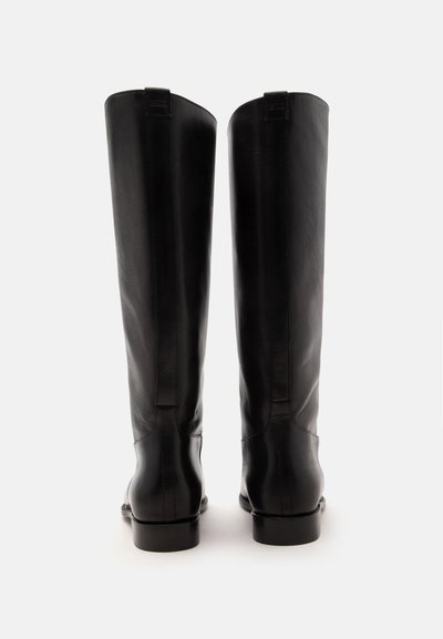 Paire de bottes en cuir noir hautes montrées de dos avec des talons bas et des languettes de tirage verticales sur un fond blanc.