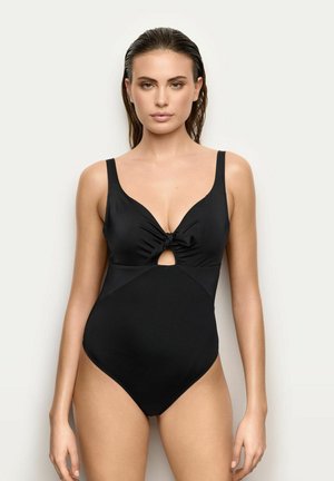 Donna con i capelli bagnati che indossa un costume intero nero con dettaglio annodato sul davanti e un piccolo taglio sotto il seno.