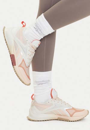 Lekkie sneakersy Reebok w białym i jasnoróżowym kolorze z panelami siateczkowymi, teksturowanymi podeszwami i pomarańczowymi akcentami, połączone z białymi skarpetkami z logo.