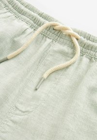 Shorts vert clair en matériau doux avec une taille élastique. Dotés d'un cordon de serrage crème avec des embouts métalliques et d'une texture subtile.