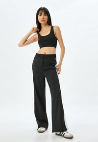 Svart sportbh och svarta vida byxor med dragsko i midjan och vita sidostrickor. Slät struktur, avslappnad atletisk design.