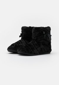 Schwarze Stiefeletten aus Kunstpelz mit einem gesteppten Design, strukturiertem Obermaterial und einer dekorativen schwarzen Schleife an der Seite. Flache Gummisohle für guten Halt.