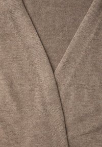 Tissu beige tricoté plié en forme de V, montrant une texture fine et douce ainsi que des coutures subtiles le long des bords.