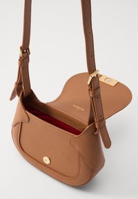 Bolsa de couro castanho com um design estruturado, alça ajustável, fechos em ouro, forro interior vermelho e um fecho magnético circular.