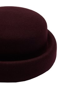 Okrągły burgundowy kapelusz wykonany z filcu, z gładką powierzchnią i szerokim, zaokrąglonym rondem. Brak widocznych elementów metalowych lub wzorów.