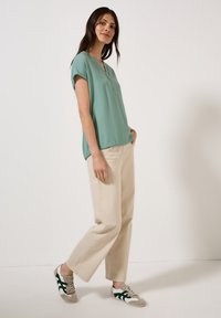 Blouse verte menthe à manches courtes et ample, associée à un pantalon large beige et des baskets multicolores avec des accents verts.