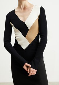 Maglione a maniche lunghe in nero, bianco e beige. Presenta un collo a V e un design a blocchi di colore geometrico con texture a coste.