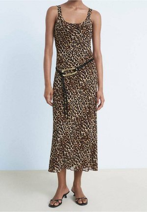 Femme portant une robe sans manches à imprimé léopard avec une ceinture tressée noire et des sandales noires à talons bas et lanières, debout sur un sol uni.